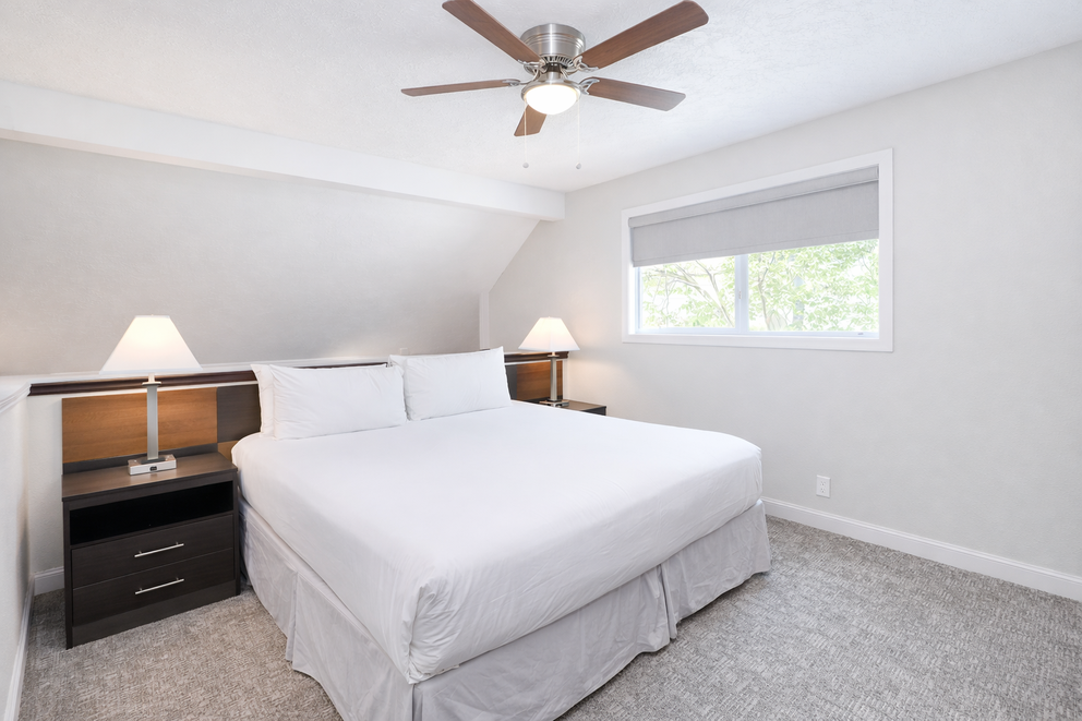 a white bed with a ceiling fan and a window