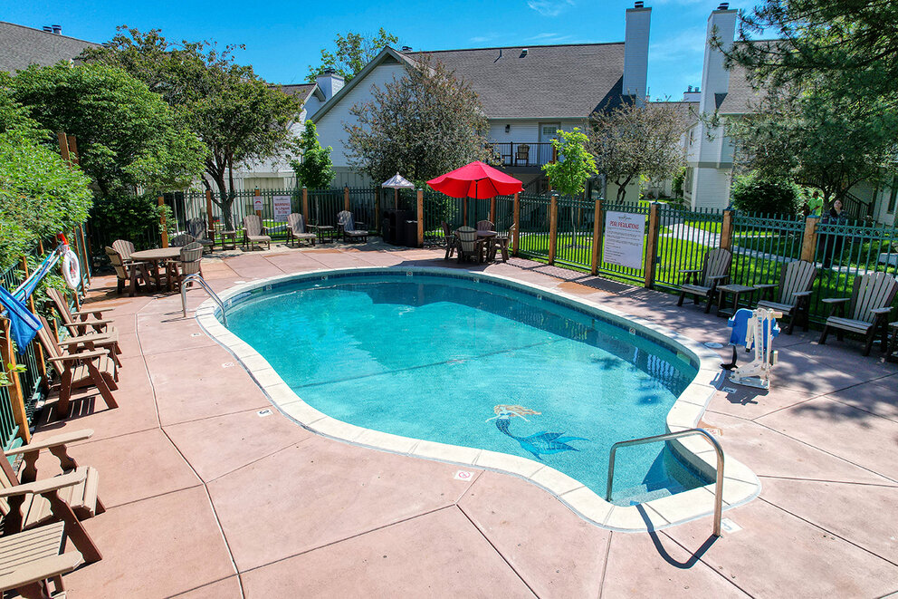 a pool with chairs and umbrellas in a backyard